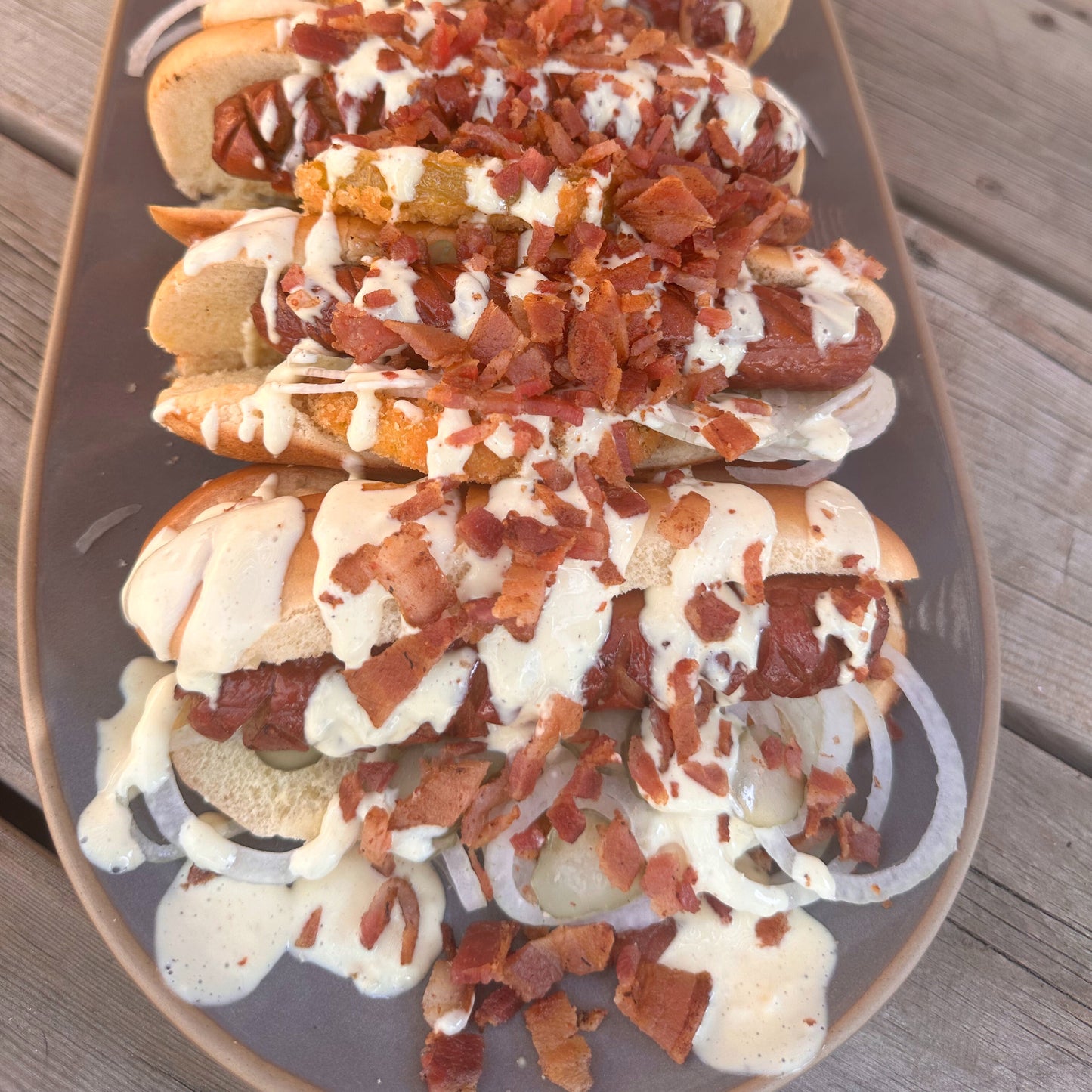 a platter of smoked and grilled hot dog with Alabama white sauce and bacon bits