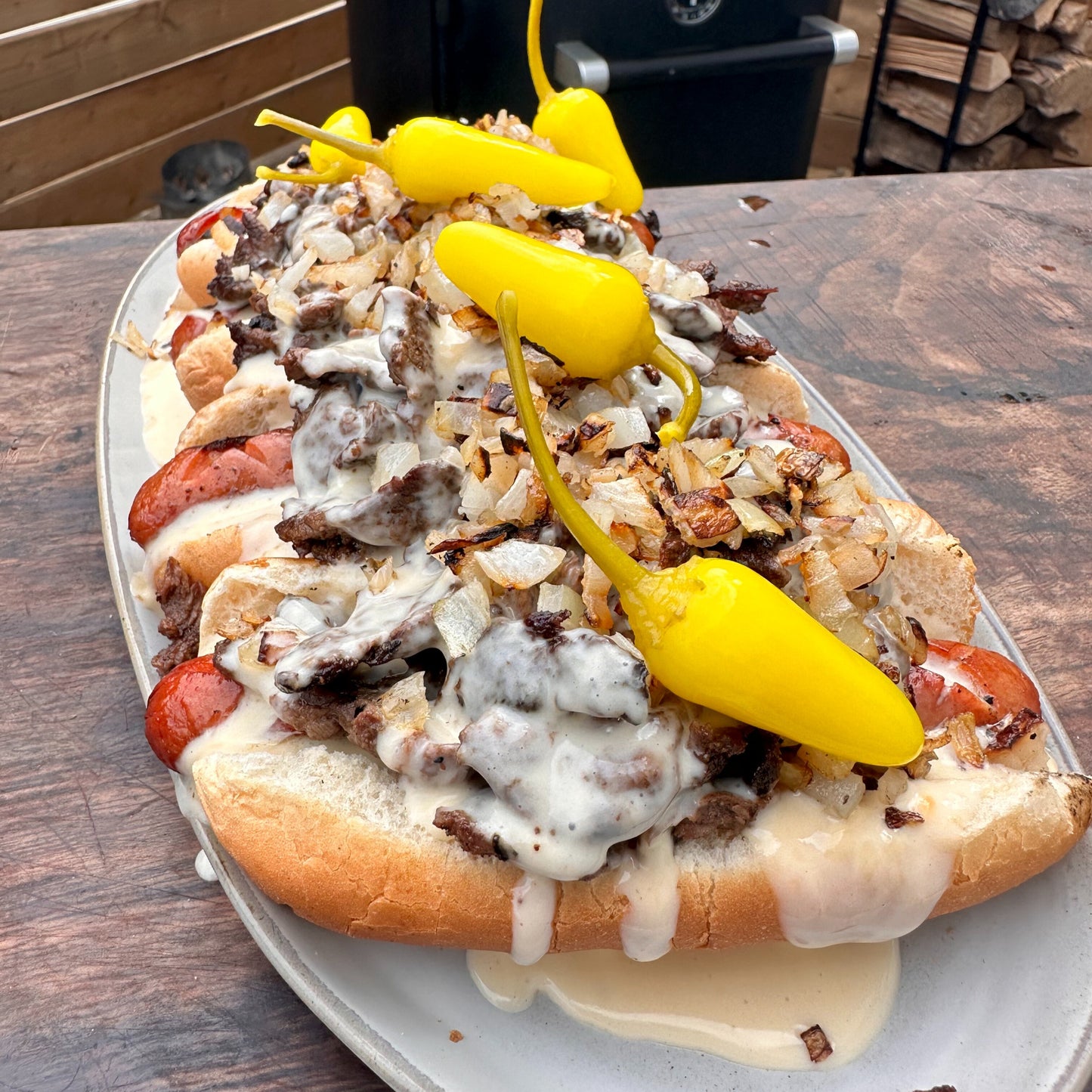 a platter of philly cheesesteak hot dogs with cheese sauce on top, grilled onions and pepperoncini peppers