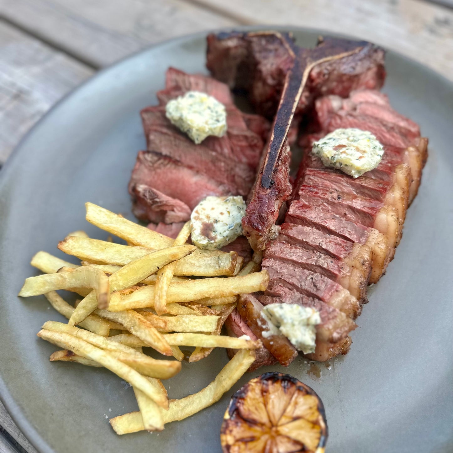 a smoked and seared porterhouse steak sliced on a platter with fries