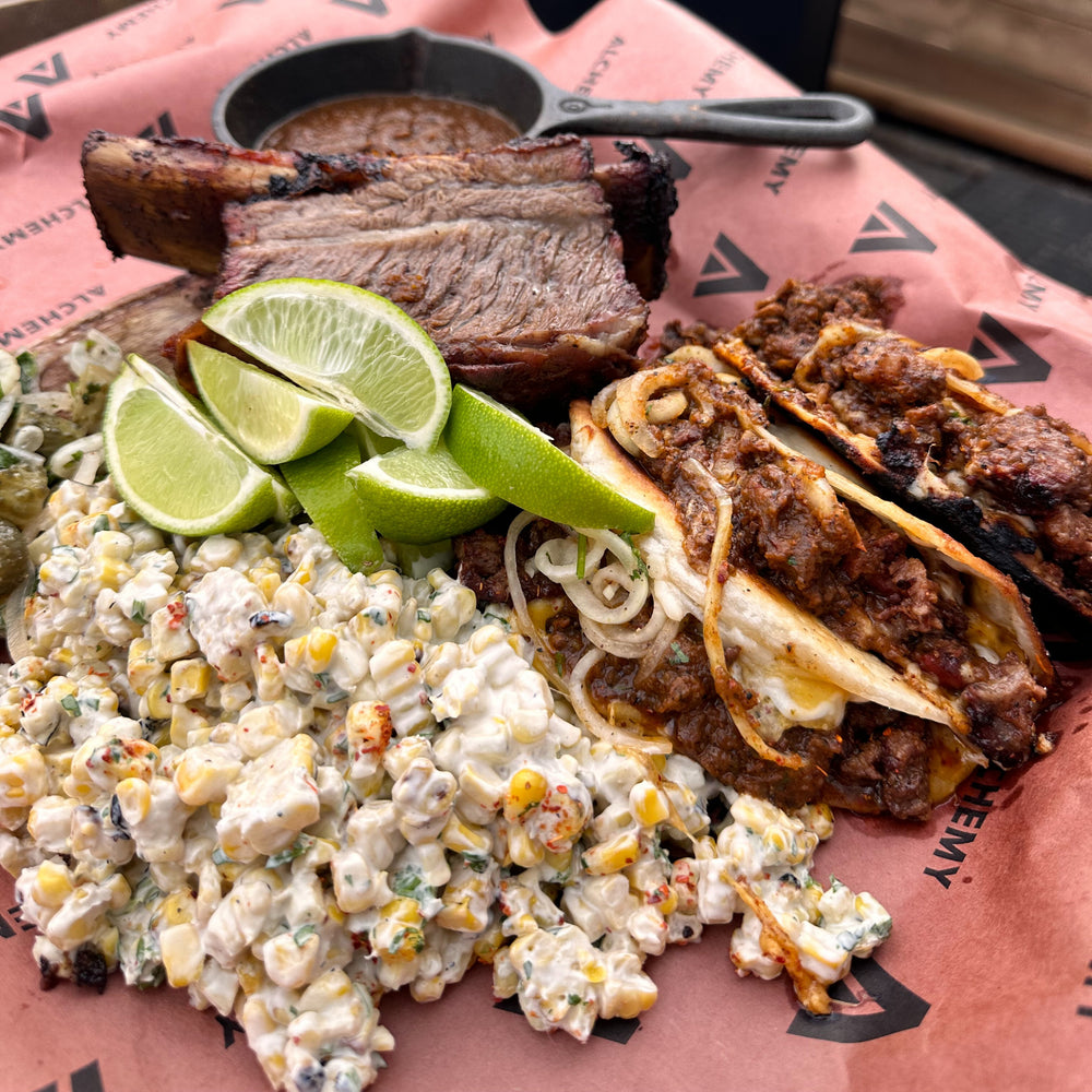 a platter with a whole smoked beef short rib, short rib tacos and elote corn salad