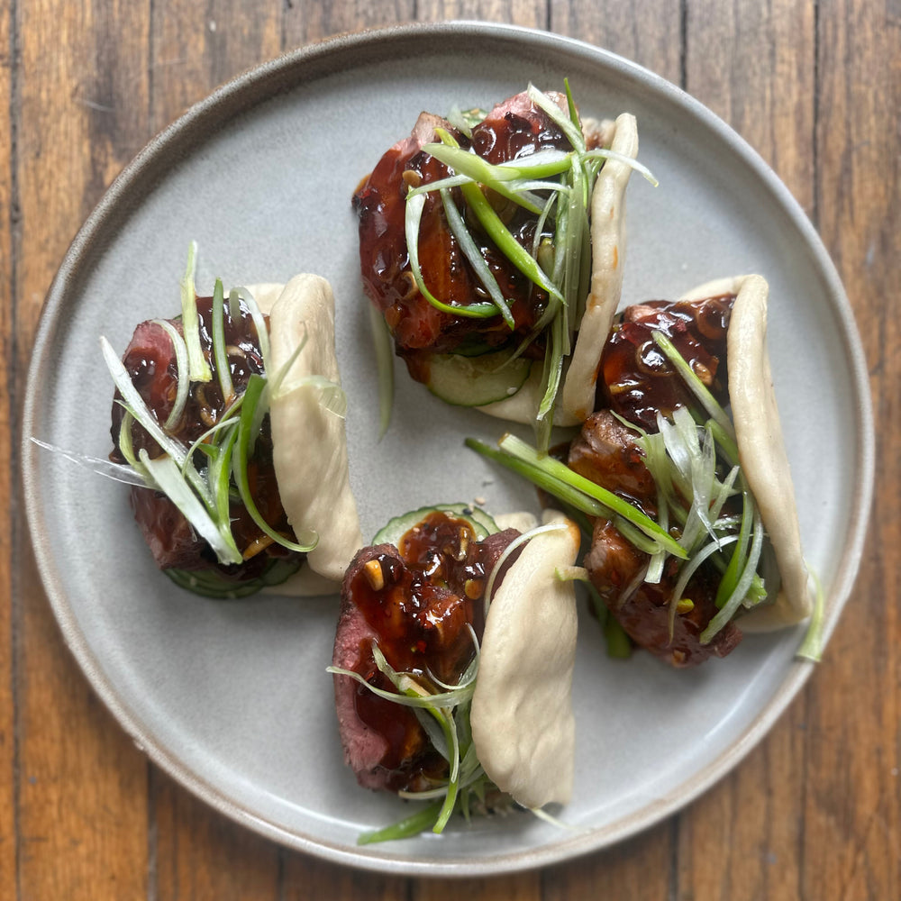 a plate of smoked duck baos with hoisin sauce, cucumber and green onion